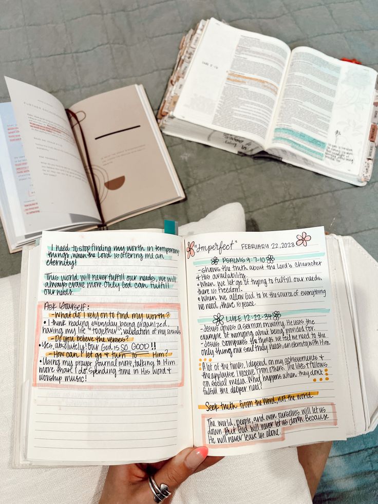 a person holding an open book on top of a white bed next to other books