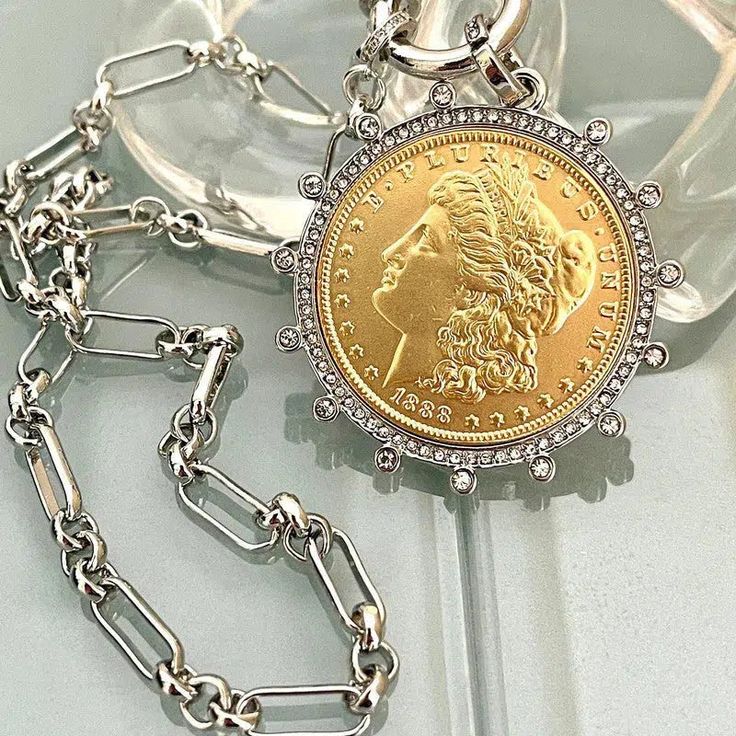 Silver Chain Necklace Beautiful reproduction vintage gold coin pendant, Morgan Peace Dollar coin in a silver bezel with cubic zirconia stones. The bale attached to the coin is also encrusted with CZ stones. The coin is 22k gold plated and elegantly hangs from a multi link Rhodium plated brass chain and a spring lock CZ clasp The spring lock closure not only makes it easy to open and close the necklace for those with difficulty but adds to the creativity of the jewelry piece. Will enhance any out Gold Coin Pendant, Silver Coin Necklace, Peace Dollar, Gold And Silver Coins, Dollar Coin, Outfit Jeans, Gold Coin, Coin Jewelry, Silver Dollar