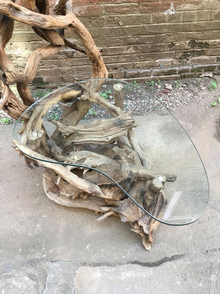 a glass table made out of driftwood on the ground next to a brick wall