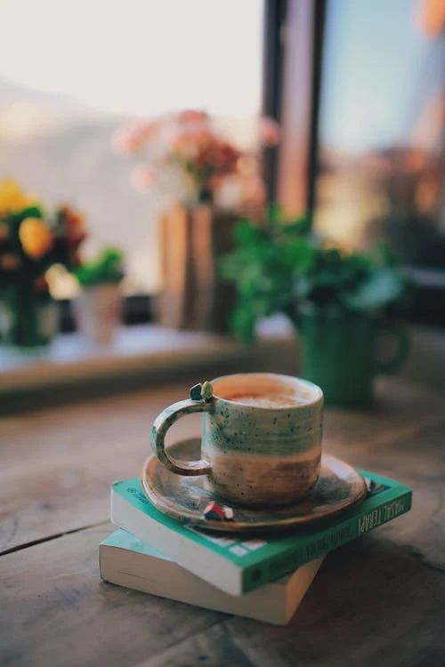 a stack of books sitting on top of a wooden table next to a coffee cup