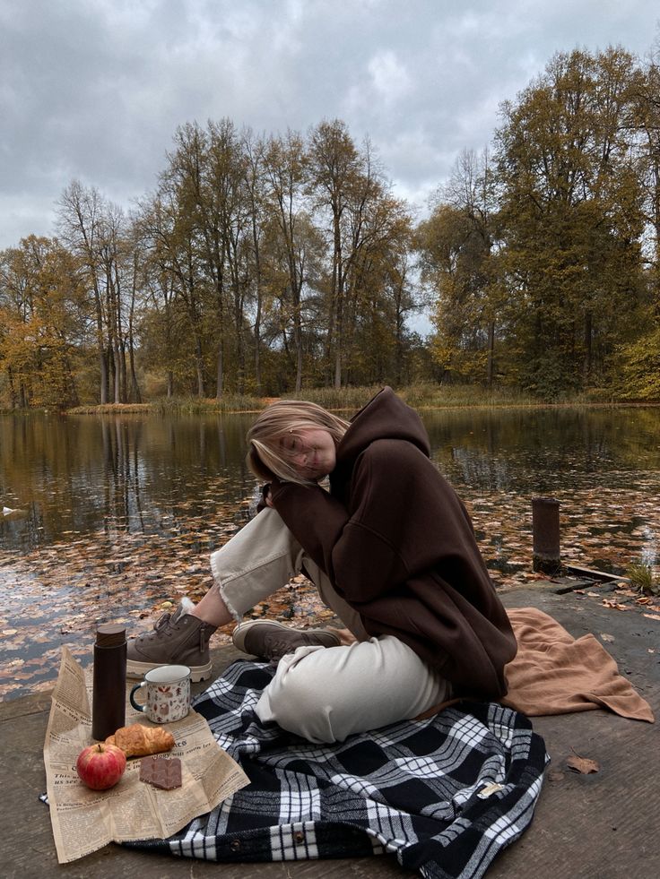 a woman sitting on the ground next to a lake with an apple in her hand