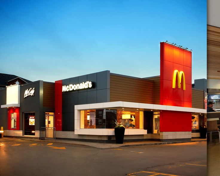 a mcdonald's restaurant is lit up at night with people walking around the building