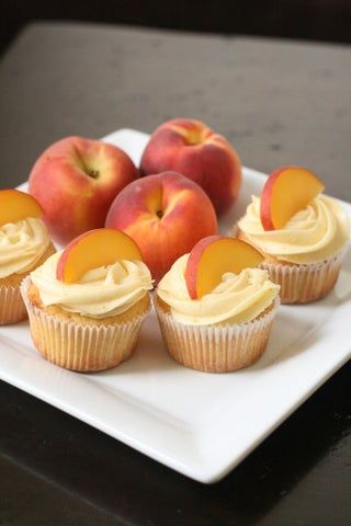 cupcakes with frosting and peaches on a square white plate, ready to be eaten