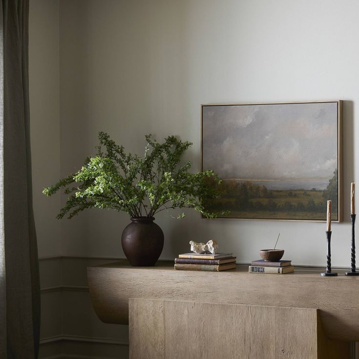 a vase with some plants on top of a wooden table in front of a painting