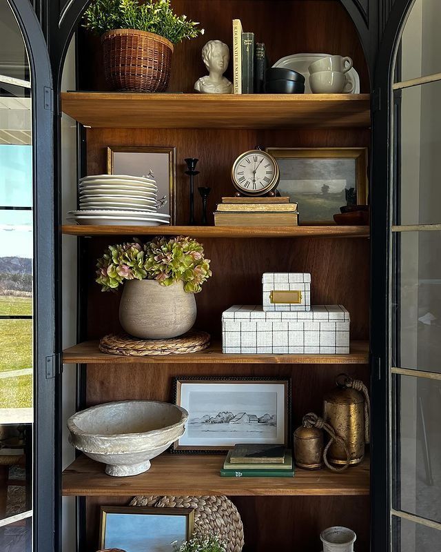 an open bookcase filled with lots of books and vases on top of it