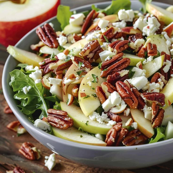 a salad with apples, cheese and pecans in a bowl on a wooden table