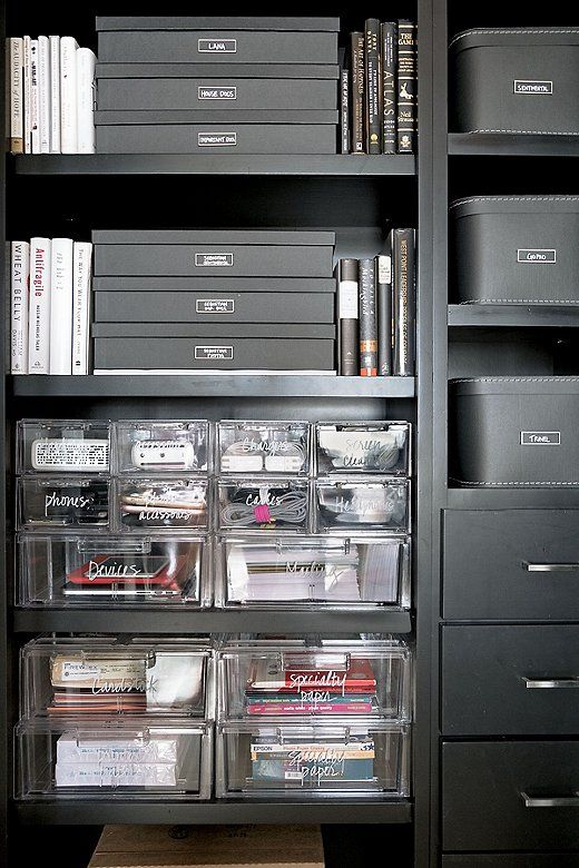 an organized bookcase filled with books and plastic bins in a home office area