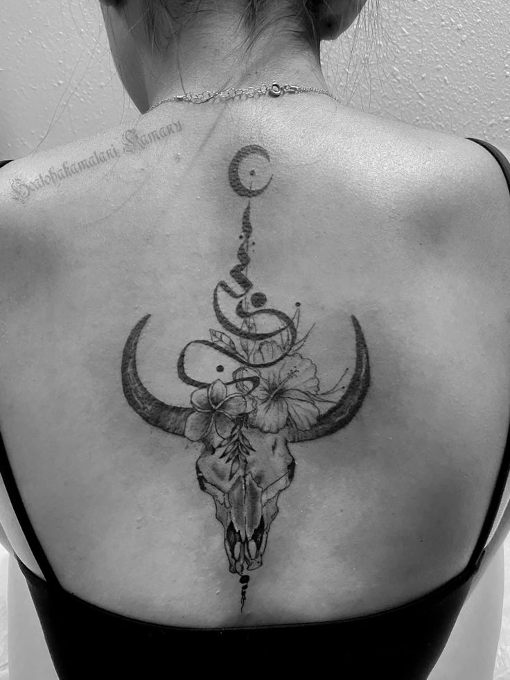 the back of a woman's shoulder with a cow skull and flowers on it