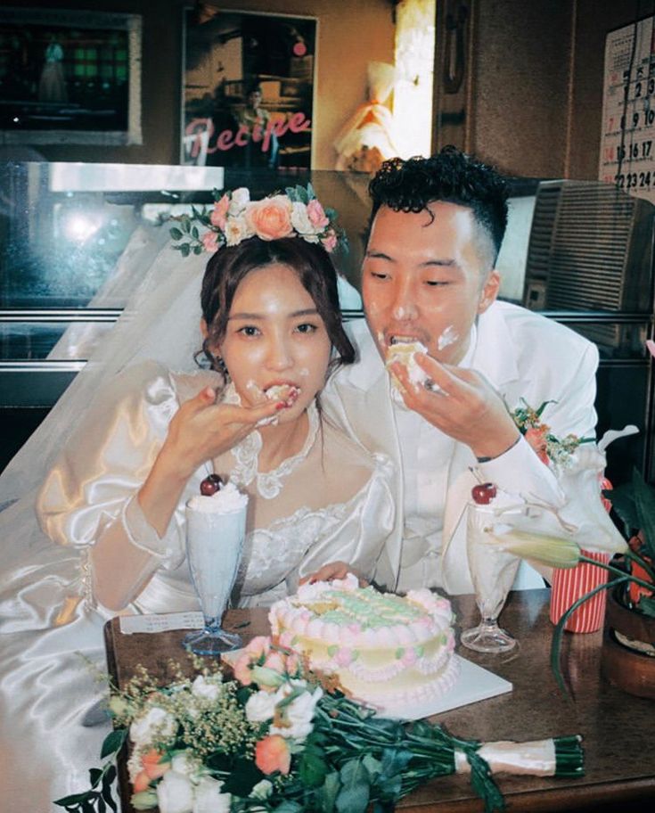 a bride and groom sitting at a table with cake in front of their faces,