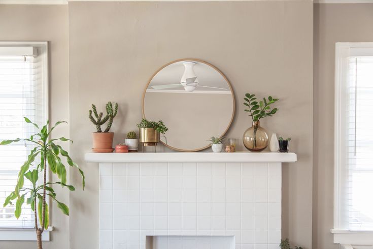 a living room with a fireplace, mirror and potted plants on the mantel