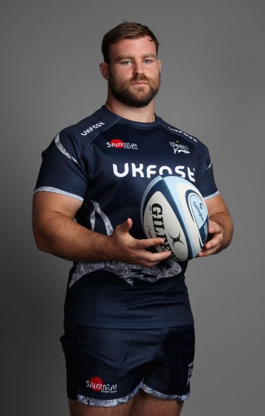 a man holding a rugby ball and posing for the camera with his hands on his hips