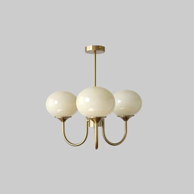 three light chandelier with white glass balls hanging from it's brass frame