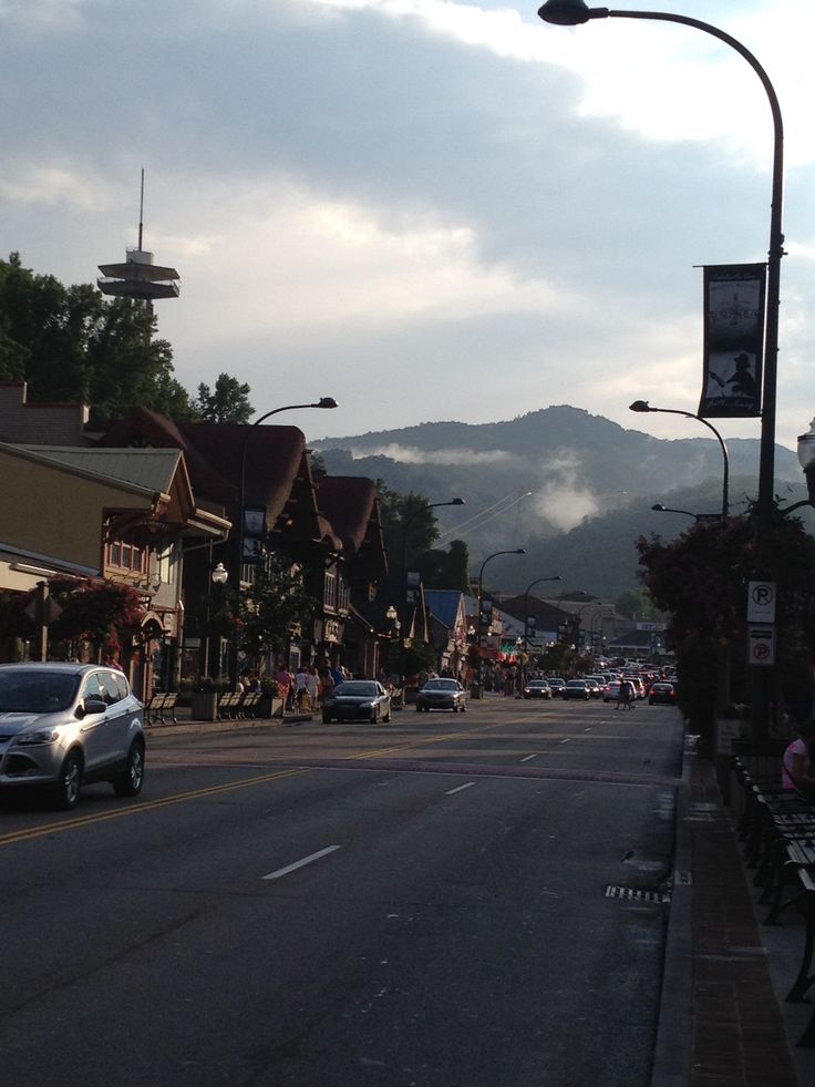 cars are driving down the street in front of shops and buildings with mountains in the background