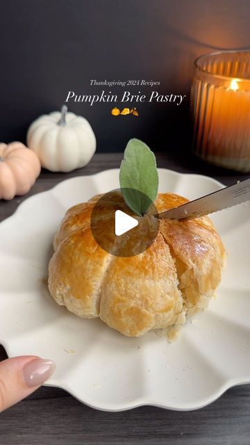 a person holding a knife over a pastry on a plate with a candle in the background