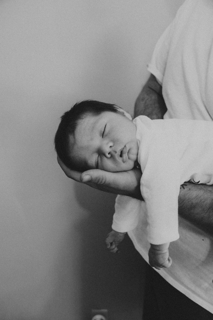 a black and white photo of a baby sleeping on his father's arm,