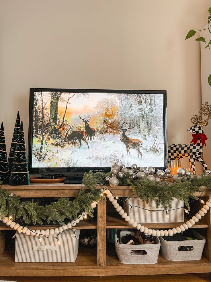 a christmas scene with deer in the snow and pine trees on top of a tv stand