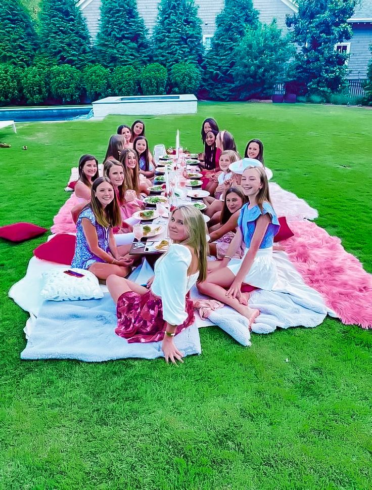 a group of young women sitting on top of a lush green field next to each other