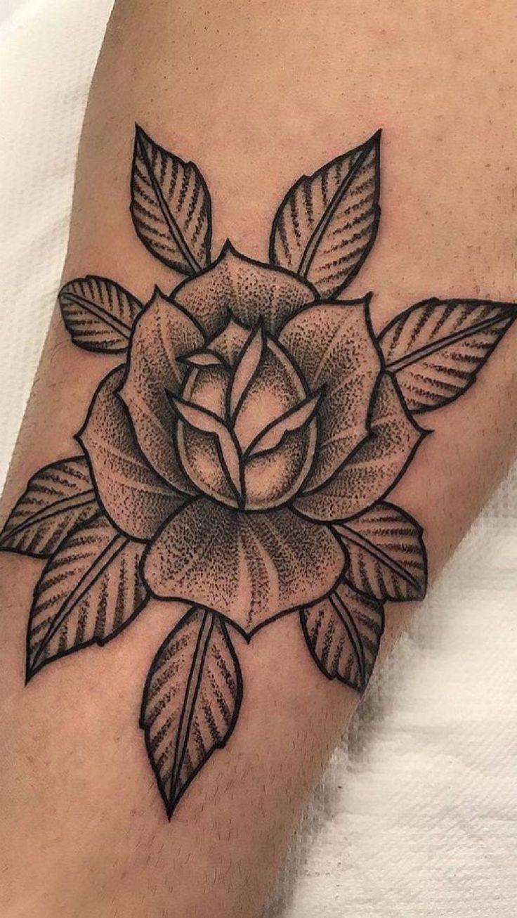 a black and white rose tattoo on the leg, with leaves around it's petals