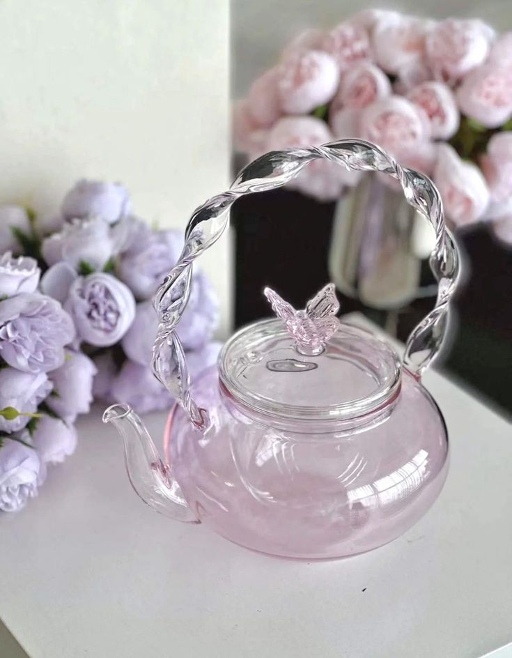 a glass tea pot sitting on top of a table next to purple flowers and a vase