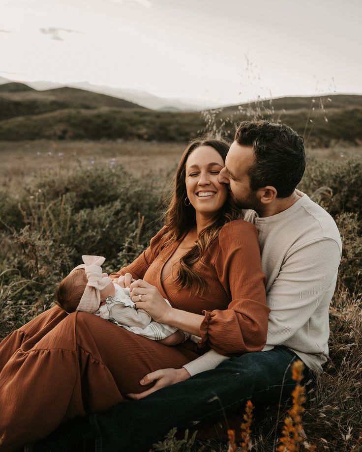 a man and woman holding a baby while sitting in a field