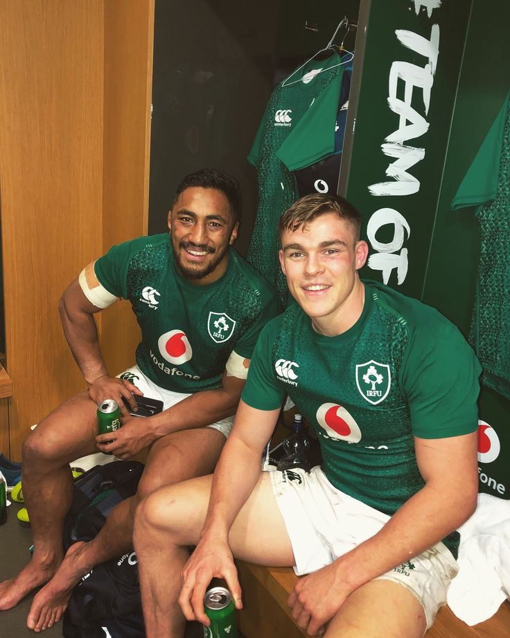 two men in green jerseys sitting next to each other with beer bottles on their laps