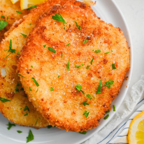 two fried fish patties on a white plate with lemon wedges and parsley