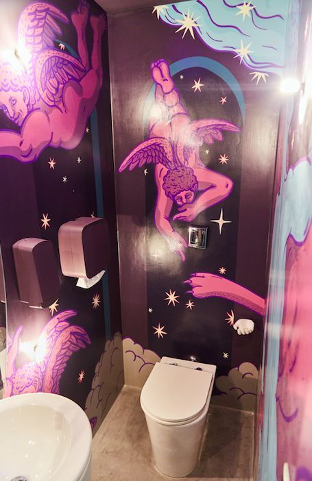 a bathroom decorated in pink and purple with an angel painted on the wall above the toilet