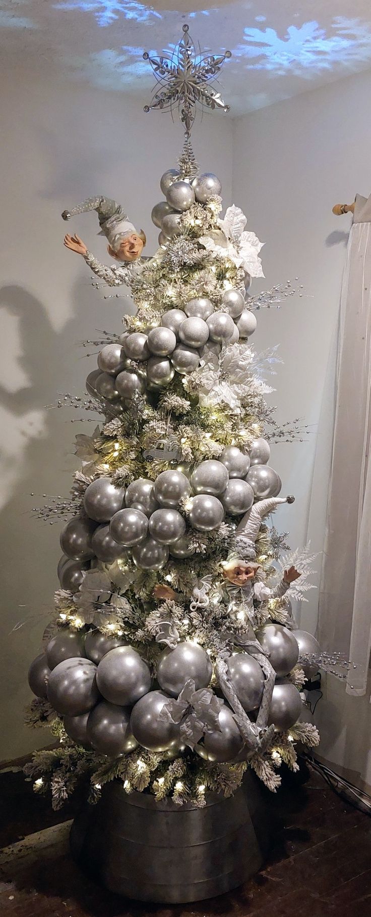 a silver and white christmas tree with ornaments on it's base in a room