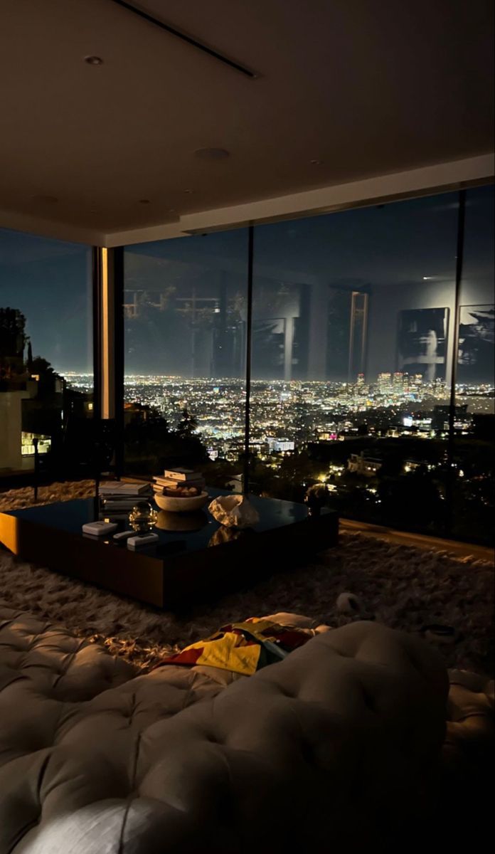 a living room filled with lots of furniture and large windows overlooking the city at night