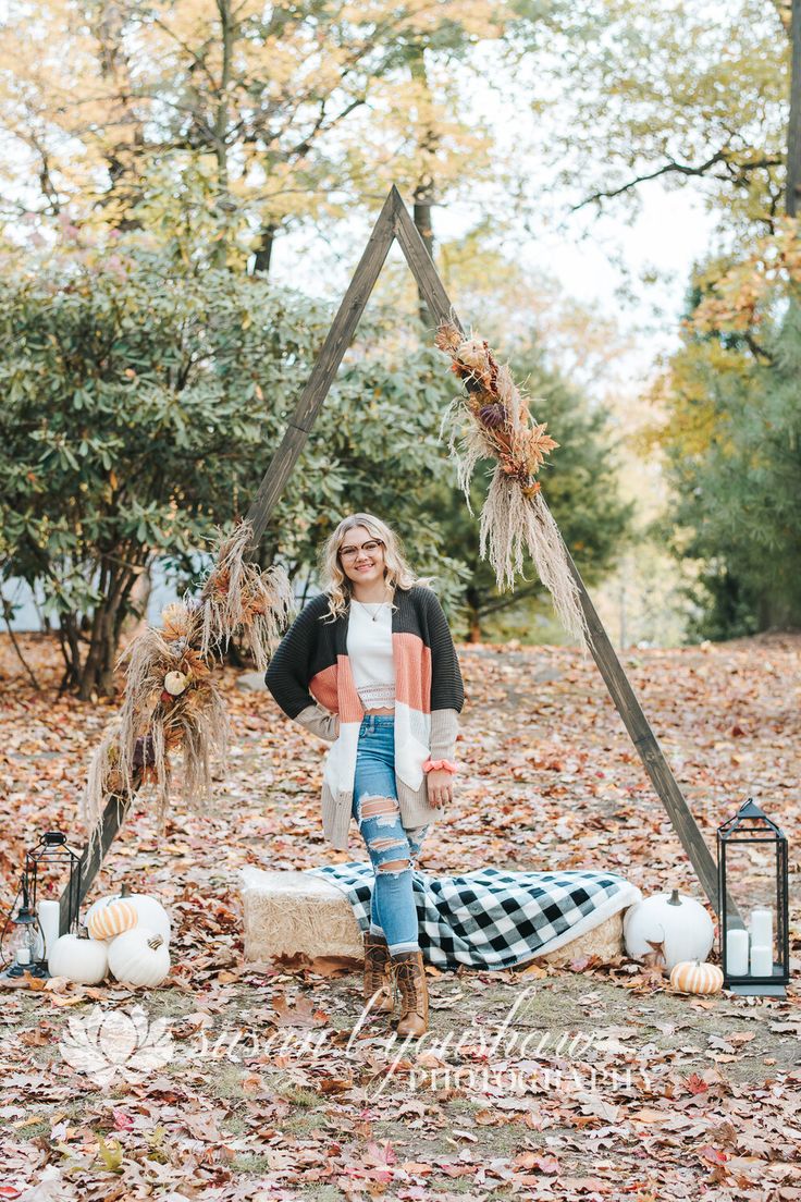 a woman is standing in the leaves near a teepeel and some pumpkins