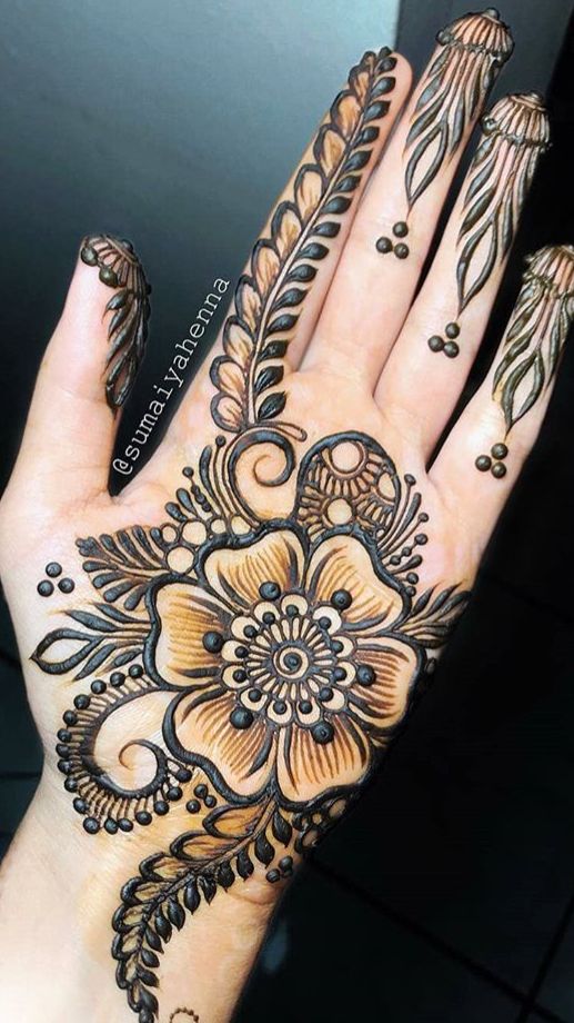 a woman's hand with henna tattoos and flowers on the top of it