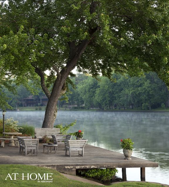 an outdoor table and chairs on a dock by the water with trees in the background