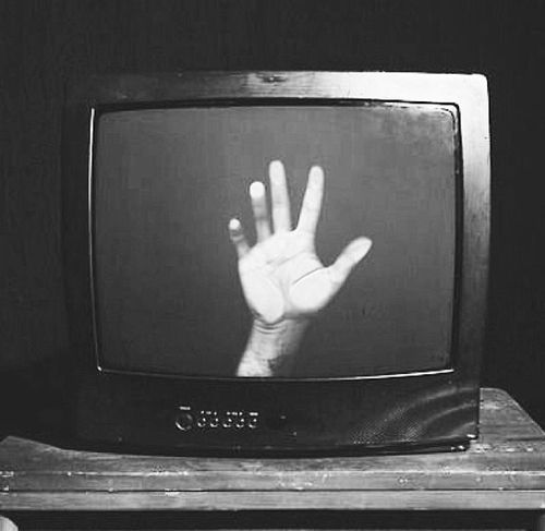 black and white photograph of hand on television screen with two hands raised up in the air