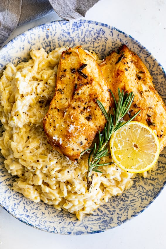 chicken and rice with lemon wedges on a blue and white plate next to a gray napkin