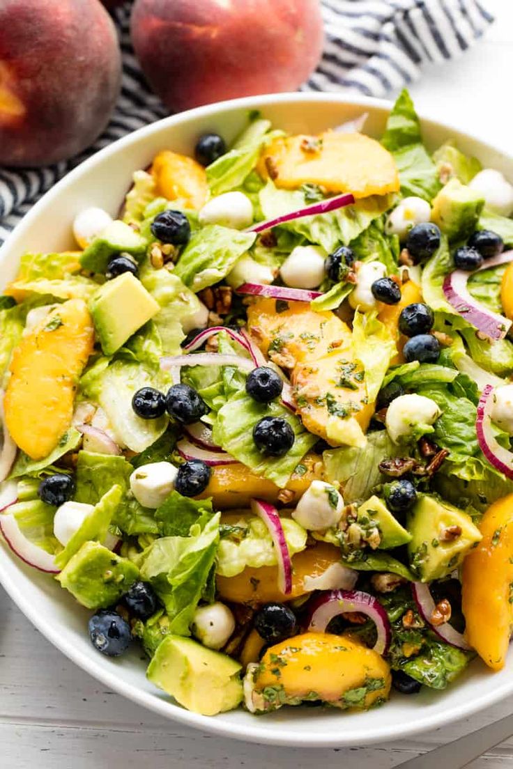 a white bowl filled with fruit and salad on top of a table next to two peaches