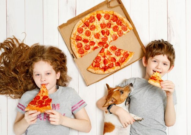 two children are eating pizza with their dog