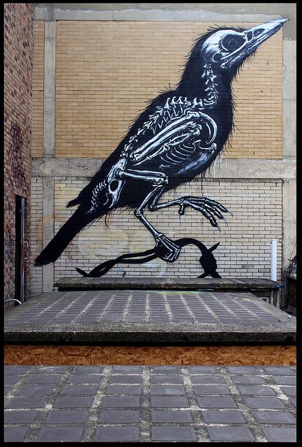 a painting of a bird on the side of a building in front of a brick wall