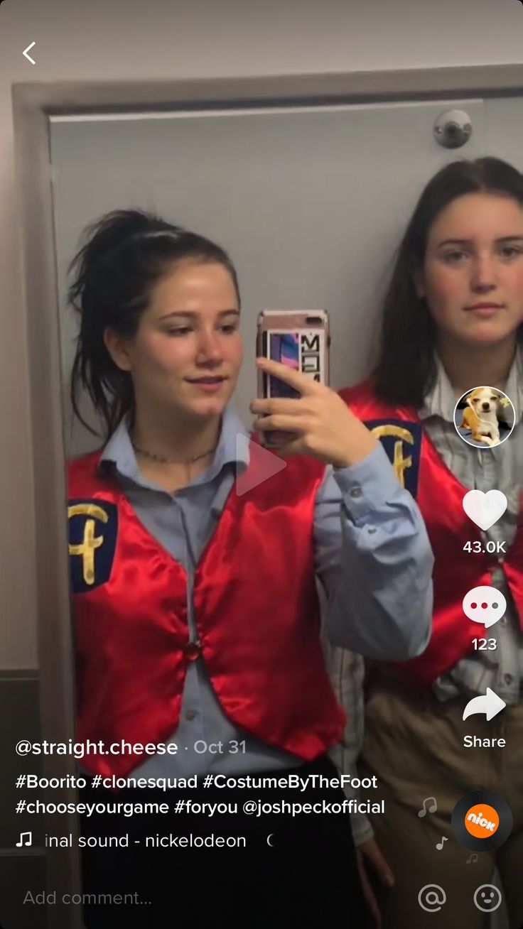 two women in red vests looking at their cell phones while standing next to each other