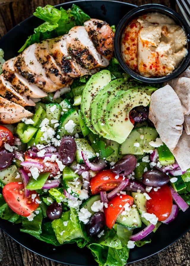 a salad with chicken, lettuce, tomatoes, cucumber, olives and feta cheese