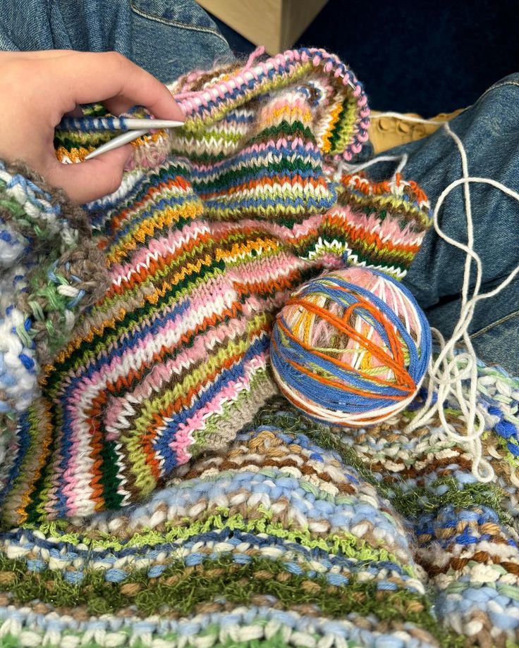 someone is knitting something on the ground with yarn in their hands and a ball of yarn next to them