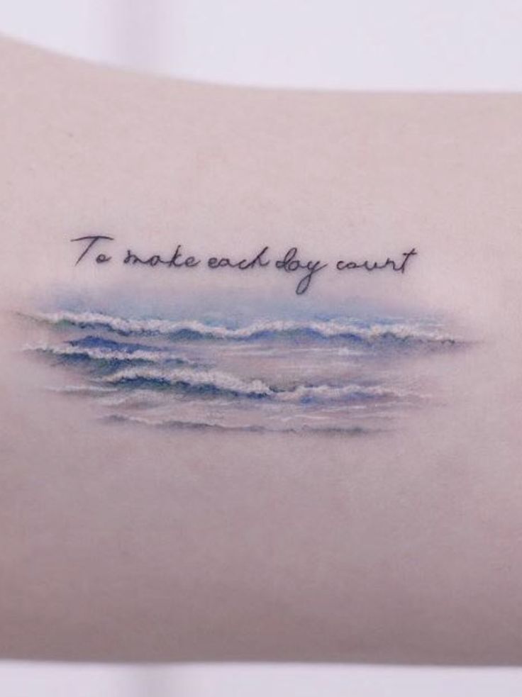 the back of a woman's shoulder with an ocean scene and words written on it