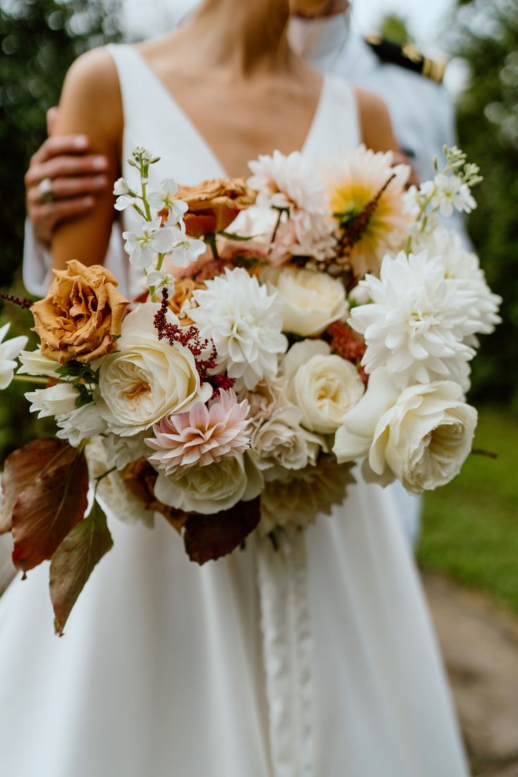 a bride holding a bouquet of white and peach flowers in front of the groom's face