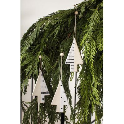 christmas decorations hanging from the side of a wooden fence with evergreen branches and white houses