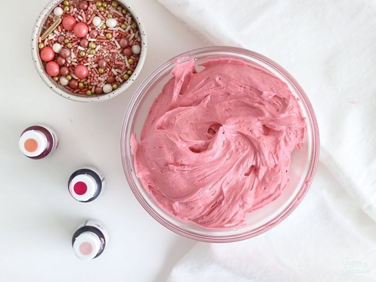 two bowls filled with pink whipped cream next to eggs and sprinkles on a white surface