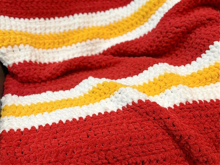 a red, yellow and white crocheted blanket sitting on top of a couch