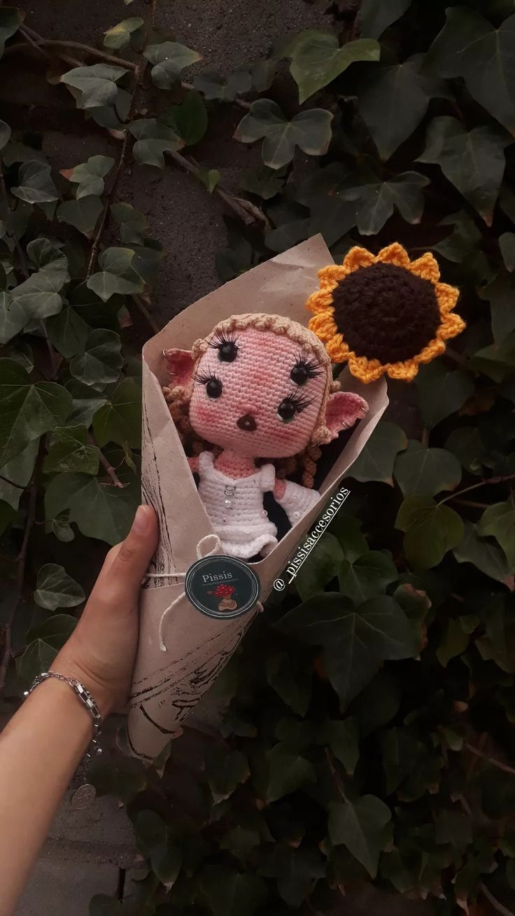 a hand holding a stuffed animal with a sunflower on it's head in a wrapper