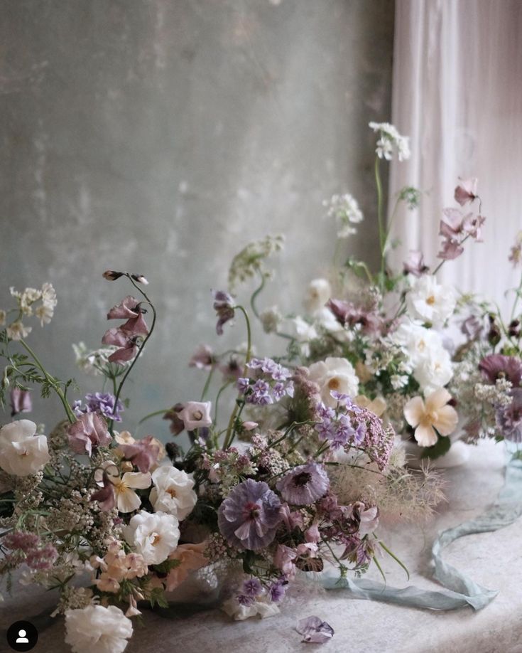 three vases filled with different types of flowers on a window sill next to a curtain