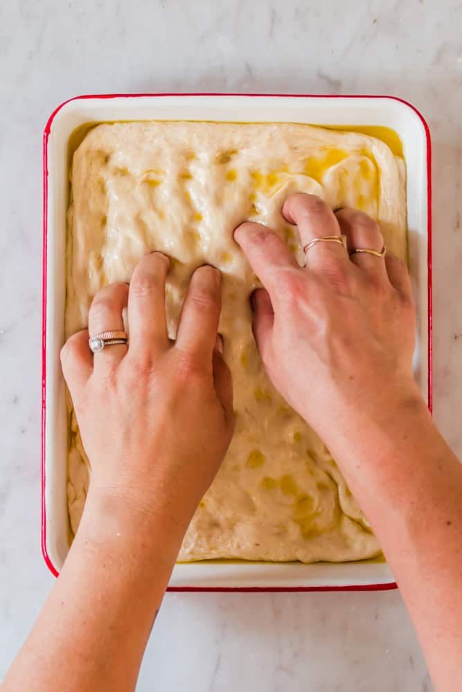 two hands reaching into a casserole dish with batter on it and another hand grabbing the top