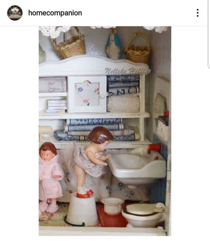 a dollhouse bathroom with two dolls playing in the sink and on the toilet basin