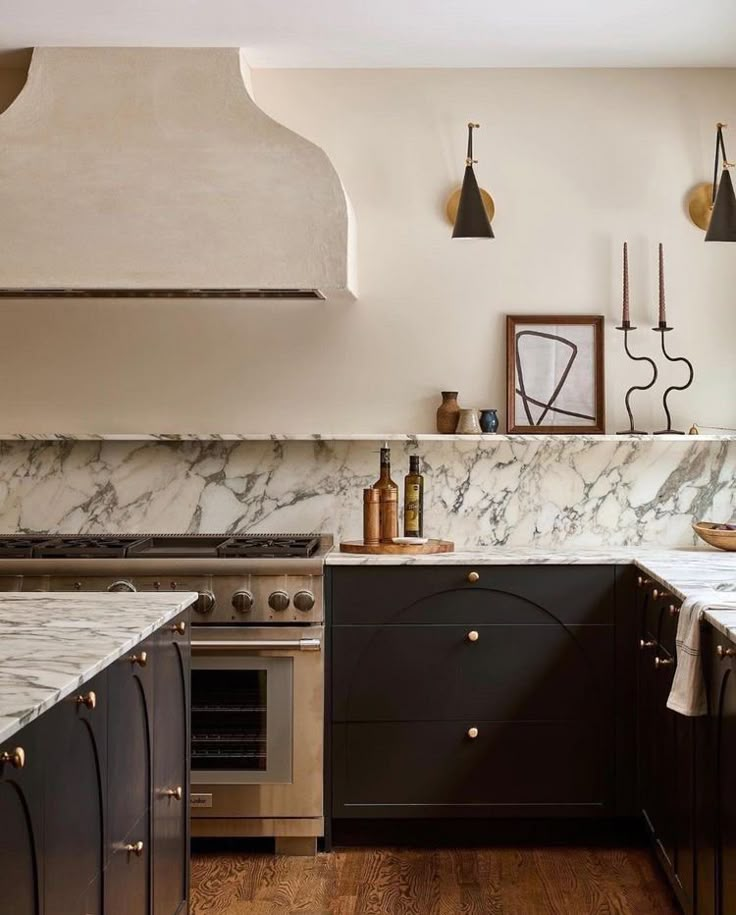 a kitchen with marble counter tops and black cabinets, along with an oven hood over the range